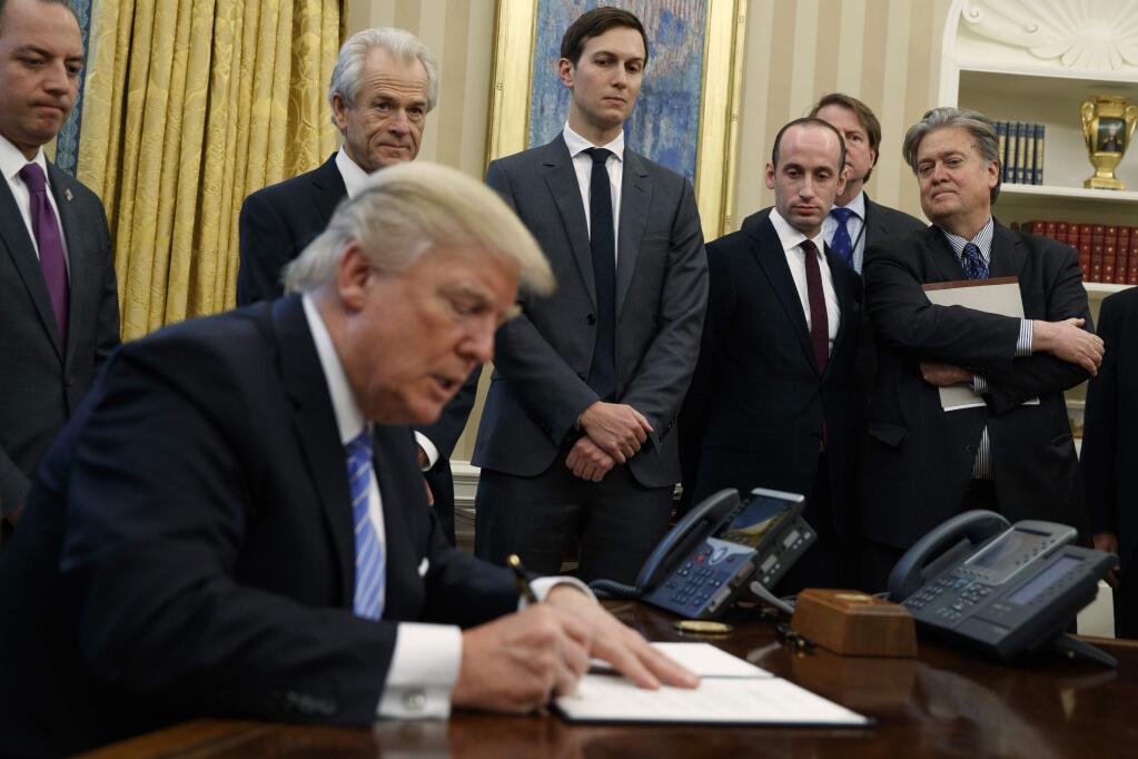 FILE - In this Jan. 23, 2017 file photo, White House chief strategist Steve Bannon, right, and others, watch as President Donald Trump signs an executive order in the Oval Office of the White House in Washington. President Donald Trump is distancing himself from chief strategist Steve Bannon, a move that has Bannon's friends and allies worried the White House is about to lose its most important populist voice. (AP Photo/Evan Vucci, File)