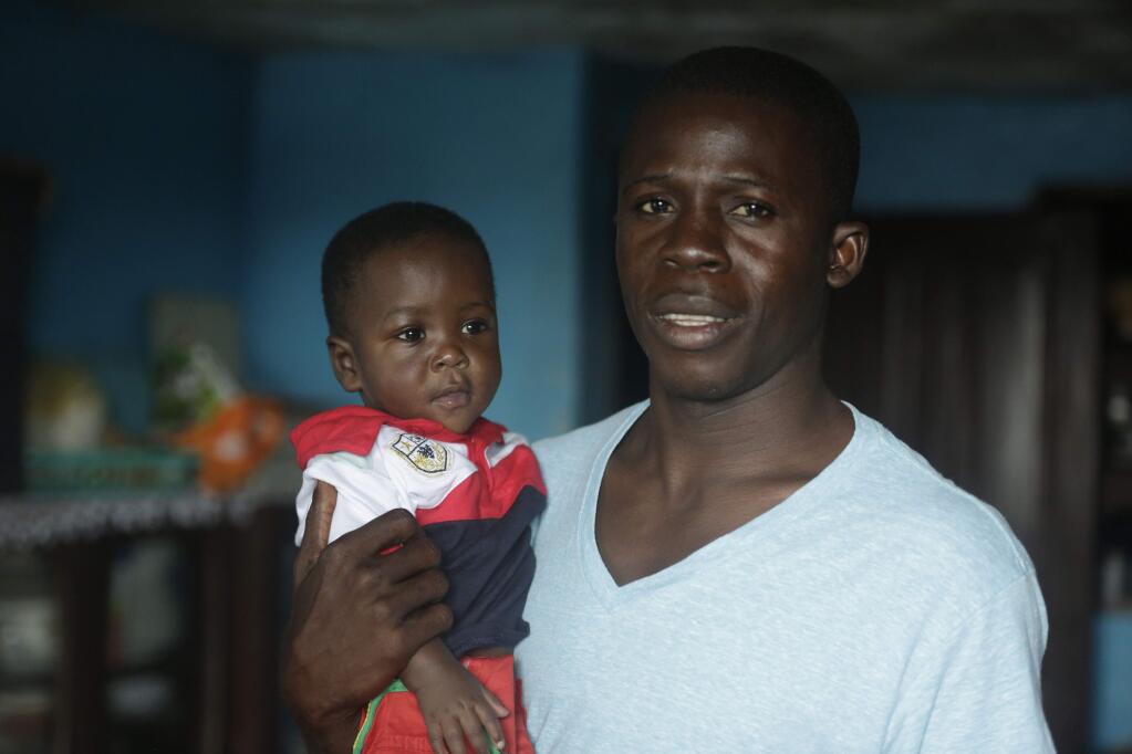 In this photo taken Tuesday, Aug. 18, 2015, nurse Donnell Tholley, 25, holds his adopted son Donnell Junior at their apartment in Freetown, Sierra Leone, as the babys great-grandmother Marie looks on. Tholley adopted the boy following the death of the mother Fatu Turay last year from the Ebola virus at the hospital on the outskirts of Freetown, Sierra Leone. The Ebola epidemic killed nearly 4,000 Sierra Leoneans and left thousands of orphans. (AP Photo/Sunday Alamba)
