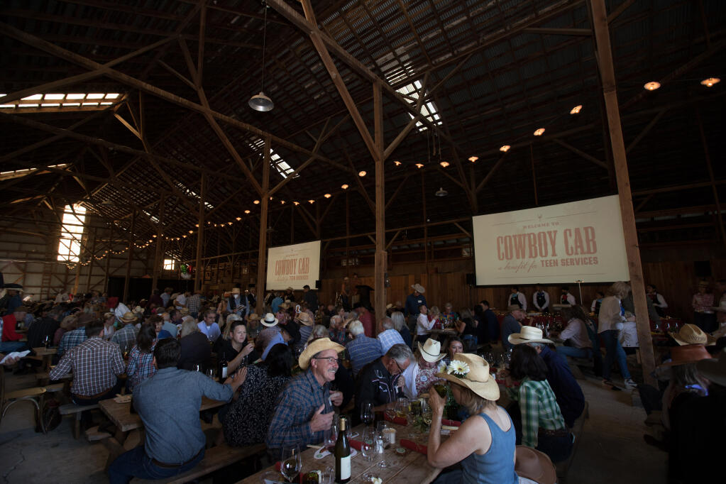 People sit down for dinner and wine at the “Cowboy Cab” benefit for Teen Services Sonoma (part of Boys and Girls Clubs of Sonoma Valley) inside Donnell Ranch Barn in Sonoma, Calif., on Saturday, May 21, 2022. (Darryl Bush/For The Press Democrat)