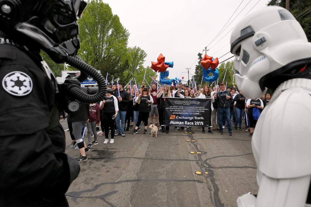 'Look at all the lightsabers, I think we're outnumbered,' says Chris Anderson, left, in costume as TIE pilot TI-42101, to Craig Gaylord, right, also know as stormtrooper TK-7776, as the lightsaber-wielding contingent from Exchange Bank approaches the starting line of the Sonoma County Human Race in Santa Rosa, California, on Star Wars Day, Saturday, May 4, 2019. (Alvin Jornada / The Press Democrat)