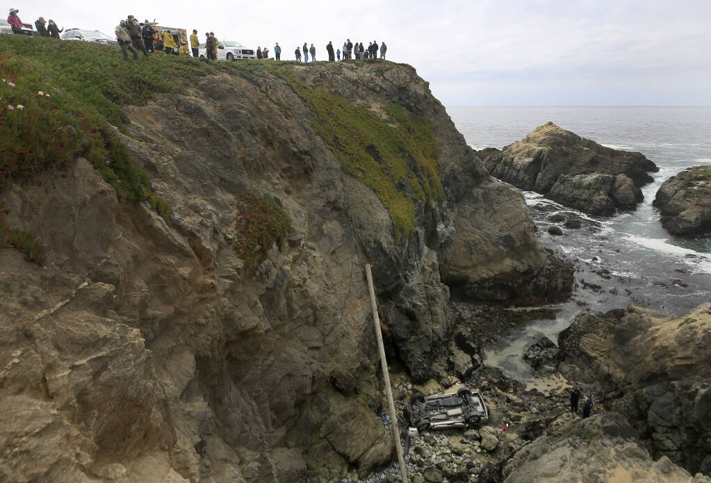 Bodega Bay firefighters work to secure the scene of a crash after a vehicle plummeted from the Bodega Head parking lot, through a wood barrier, landing upside down 100 feet to the rocky shoreline, killing two people in the SUV, Saturday, April 3, 2021. (Kent Porter / The Press Democrat)