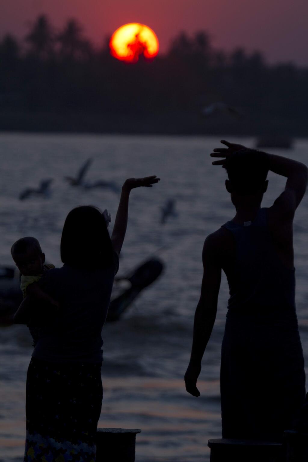 A couple with their child waves during the last sunset of the year at a jetty at Yangon river in Yangon, Myanmar Wednesday, Dec. 31, 2014. (AP Photo/Khin Maung Win)