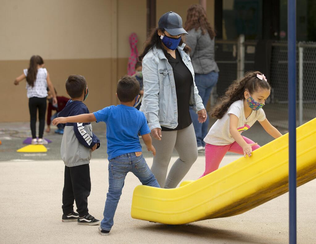 Teacher Nadia Alhaj Ali watches over children in daycare using the slide on the playground at the North Bay Children's Center at Steele Lane School in Santa Rosa on Thursday, July 23, 2020.   (Photo by John Burgess/The Press Democrat)
