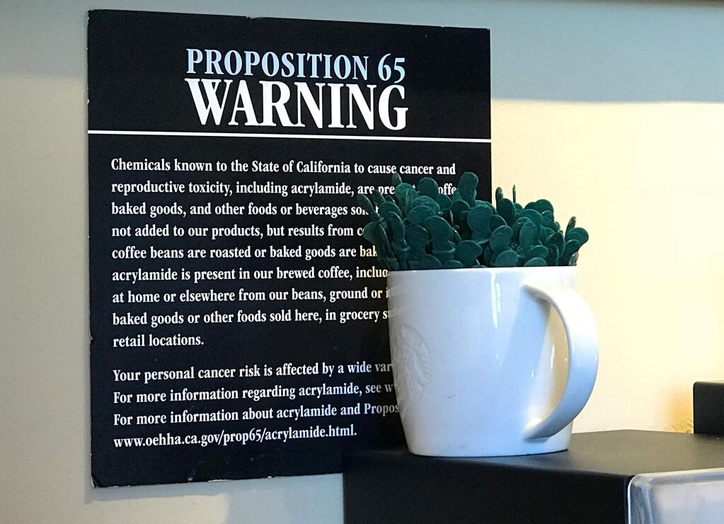 FILE - This March 30, 2018 file photo shows a Proposition 65 warning sign behind a coffee mug at a Starbucks coffee shop in Burbank, Calif. California has officially concluded coffee does not pose a 'significant' cancer risk. State regulators gave final approval Monday, June 3, 2019 to a rule that means coffee won't have to carry ominous warnings that the beverage may be bad for you. (AP Photo/Damian Dovarganes, File)