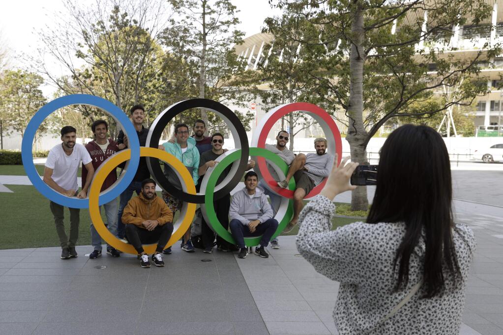 A group of students from Uruguay pose for a souvenir picture on the Olympic rings outside the Olympic Stadium in Tokyo, Saturday, March 21, 2020. The Olympic flame from Greece arrived in Japan Friday, even as the opening of the the Tokyo Games in four months is in doubt with more voices suggesting the games should to be postponed or canceled because of the worldwide virus pandemic. (AP Photo/Gregorio Borgia)