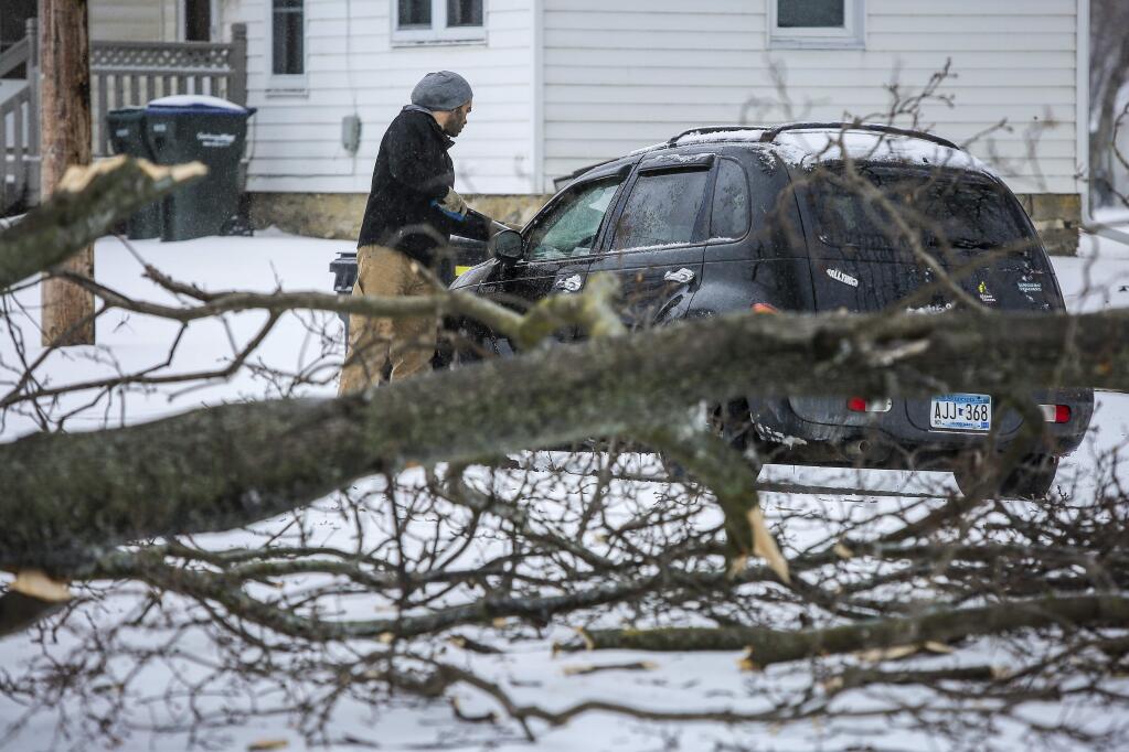 Lee Rinehart scrapes snow and ice off of his vehicle near where a large tree branch had fallen during a storm Saturday, April 14, 2018, in Rochester, Minn. A storm system stretching from the Gulf Coast to the Great Lakes buffeted the central U.S. with heavy winds, rain, hail and snow, (Joe Ahlquist /The Rochester Post-Bulletin via AP)