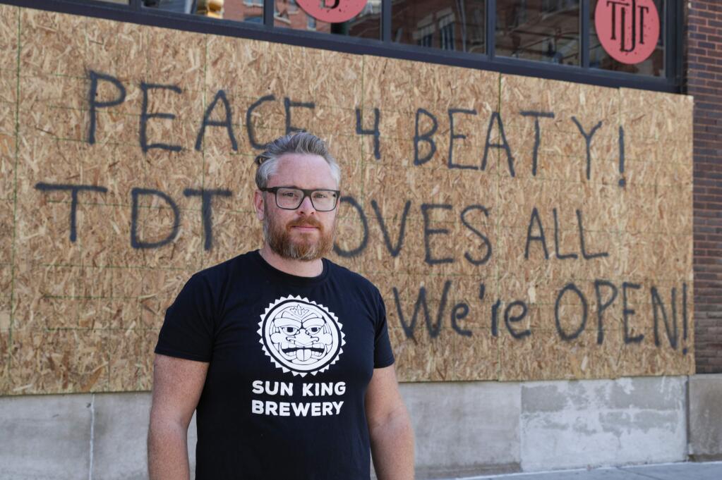 Restaurant owner Michael Cranfill poses in front of sign on the restaurant's boarded up windows in Indianapolis, Tuesday, June 2, 2020 to honor his friend former Indiana University football player Chris Beaty. Beaty was one of two people fatally shot in Indianapolis during protests over the death of George Floyd.(AP Photo/Michael Conroy)