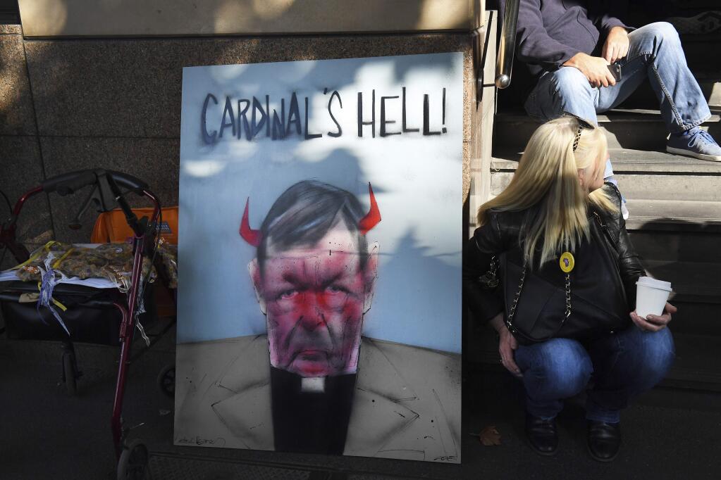 A demonstrator sits beside a placard carrying the image of Australian Cardinal Greorge Pell, outside the Melbourne Magistrate Court in Melbourne Tuesday, May 1, 2018. Australian Cardinal Pell, the most senior Vatican official to be charged in the Catholic Church sex abuse crisis, must stand trial on charges that he sexually abused multiple victims decades ago, a magistrate ruled Tuesday. (AP Photo/Andy Brownbill)