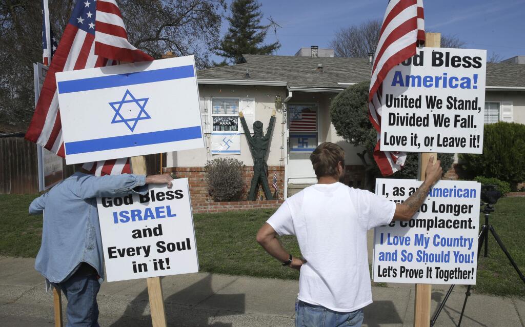 Robert Dixon, left, and Kraig Smith, demonstrate outside a home calling for removal of swastikas displayed on the home in Sacramento, Calif., Thursday Feb. 26, 2015. State lawmakers have demanded that the resident of the home remove the symbols calling the signs racist and vulgar but acknowledging the homeowner had a right to free speech. The flags show swastikas replacing stars in one American and two Israeli flags. (AP Photo/Rich Pedroncelli)
