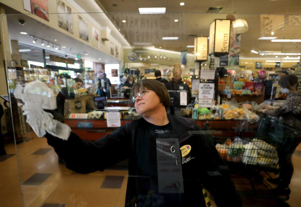 Employee Candace Rhoades cleans a new plexiglass protective barrier that has been installed in front of her register and at all the checkout counters at Oliver's Market in Santa Rosa on Tuesday, March 31, 2020. (BETH SCHLANKER/ The Press Democrat)