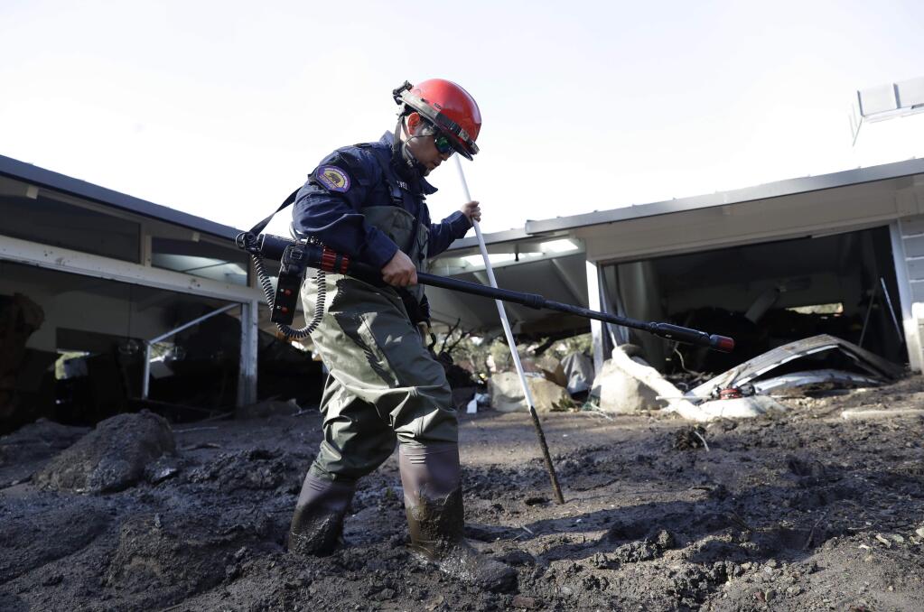 Jefferey Galvez, of the Vandenberg Fire Department Search and Rescue, walks through mud while searching in an area damaged by storms in Montecito, Calif., Friday, Jan. 12, 2018. The number of missing after a California mudslide has fluctuated wildly, due to shifting definitions, the inherent uncertainty that follows a natural disaster, and just plain human error. (AP Photo/Marcio Jose Sanchez)