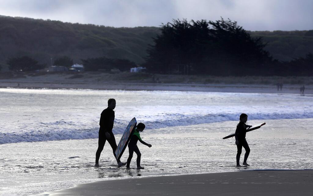 Ian Maxwell heads back into shore with boogie boarders Cael, 6 and Fiona, 8 after the fog rolled in at Doran Beach Regional Park.  (John Burgess / The Press Democrat)