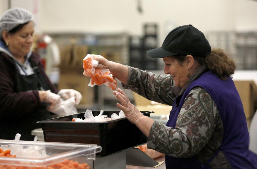 Line leader Olive Brandalick helps pack bag of individually wrapped carrots for free lunches available to TK-12 students to pick up at select school sites in Santa Rosa. Photo taken Santa Rosa City Schools Child Nutrition Services kitchen in Santa Rosa on Monday, March 23, 2020. (BETH SCHLANKER/ The Press Democrat)