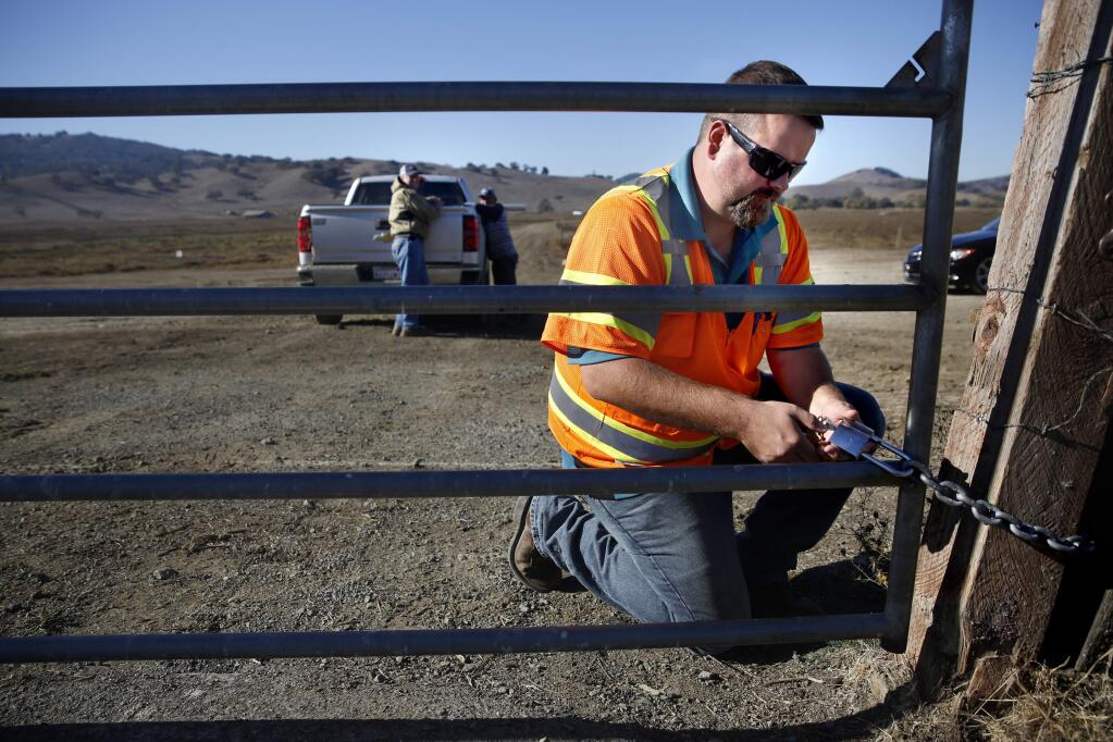 SMART controller supervisor Dennis Bush locks a gate along the SMART rail line after allowing Jerry Corda to cross the tracks in his pickup in order to feed cattle on the ranch in Petaluma, on Thursday, November 12, 2015. (BETH SCHLANKER/ The Press Democrat)