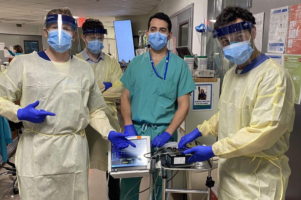 In this Monday, March 30, 2020 photo provided by Mount Sinai, from left, Drew Copeland, RPSGT; Dr. Thomas Tolbert, Dr. Brian Mayrsohn, and Dr. Hooman Poor, stand with a ventilator prototype they developed from a sleep apnea machine at Mount Sinai hospital in New York. (Mount Sinai via AP)