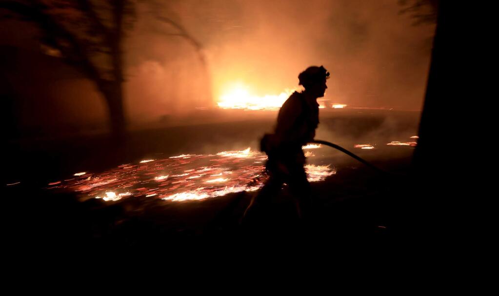A Cal Fire firefighter races to protect a structure at 1108 Bennett Lane and Highway 128 in Napa County close to the origin of the Tubbs fire, Sunday Oct. 8, 2017. The house later burned to the ground. The home was among the first to catch fire. (Kent Porter / Press Democrat) 2017