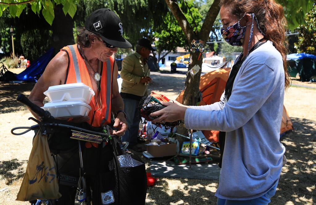 Patrick Preston gets the pick of face masks from Sheryl Rood of Sonoma Applied Village Services at a homeless camp in Fremont Park in Santa Rosa, Tuesday, July 23, 2020.  (Kent Porter / The Press Democrat) 2020