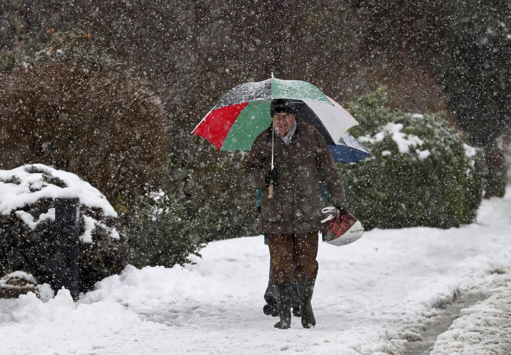 People walk through snowy conditions in Danbury, south east England, Monday Dec. 11, 2017. Snow and wintry weather are still wreaking havoc on travelers in Britain, with flights cancelled, roads sheathed in ice and rail travel disrupted. (Gareth Fuller/PA via AP)