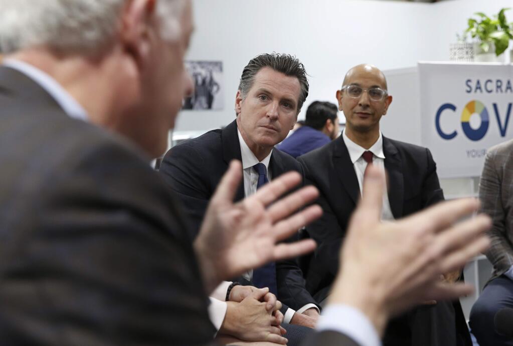 FILE - In this May 14, 2019, file photo, California Gov. Gavin Newsom, center, listens as John Arensmeyer, founder and CEO of Small Business Majority, left, discusses the problems small businesses have getting health insurance during a discussion with small business owners in Sacramento, Calif. The California Legislature approved a bill, Monday, June 24, 2019, that taxes people who refuse to buy health insurance and uses the money to help small business owners and others pay for health insurance. (AP Photo/Rich Pedroncelli, File)