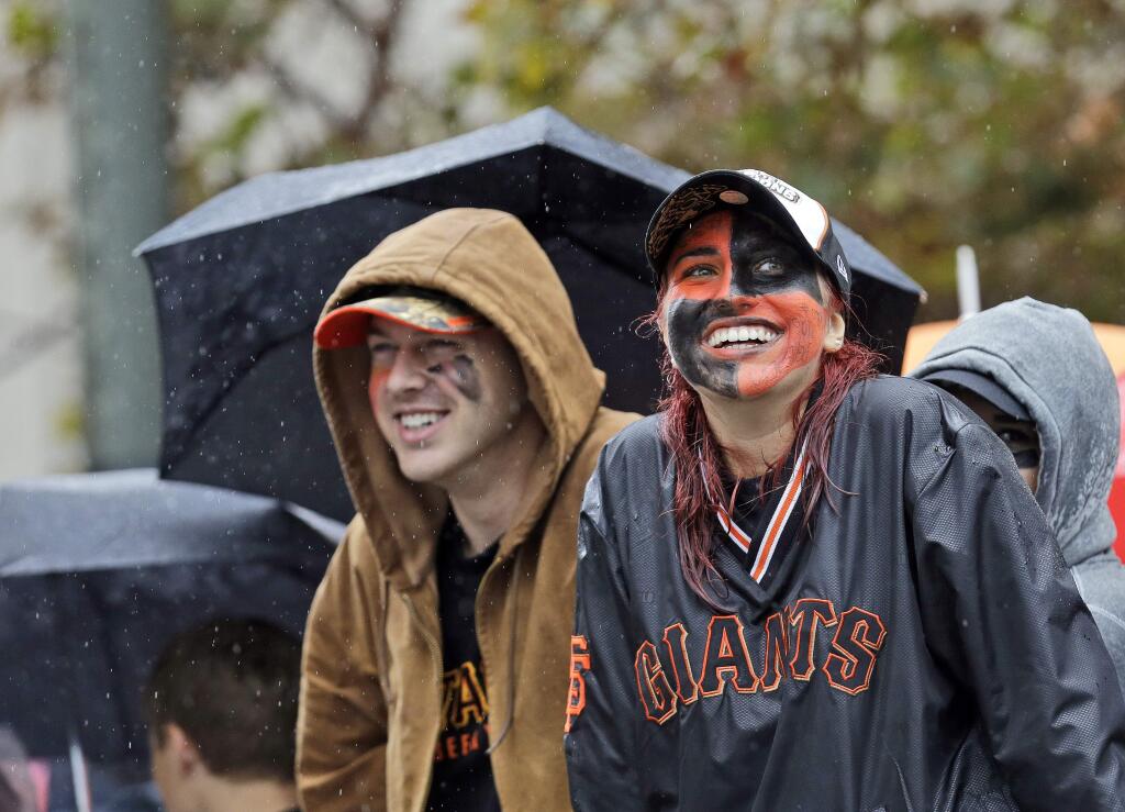 San Francisco Giants baseball fans Megan McPhillips, right, and Travis Saracco from Santa Rosa, Calif., wait in the rain for the start of the victory parade for the 2014 World Series Champion San Francisco Giants on Friday, Oct. 31, 2014 in San Francisco. (AP Photo/Jeff Chiu)