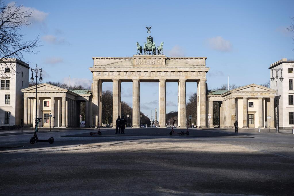Policemen stand at the Pariser Platz in front of the Brandenburg Gate in Berlin Saturday morning, March 21, 2020. The Senate announced further measures to stop the spread of the new coronavirus in Berlin. For most people, the new coronavirus causes only mild or moderate symptoms. For some it can cause more severe illness. (Paul Zinken/dpa via AP)