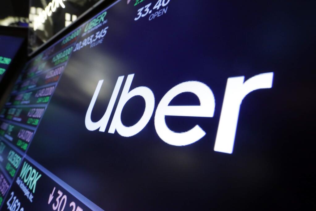 FILE - In this Aug. 16, 2019 file photo, the logo for Uber appears above a trading post on the floor of the New York Stock Exchange. Uber has cut 3,000 jobs from its workforce, its second major wave of layoffs in two weeks as the coronavirus slashed demand for rides. (AP Photo/Richard Drew, file)