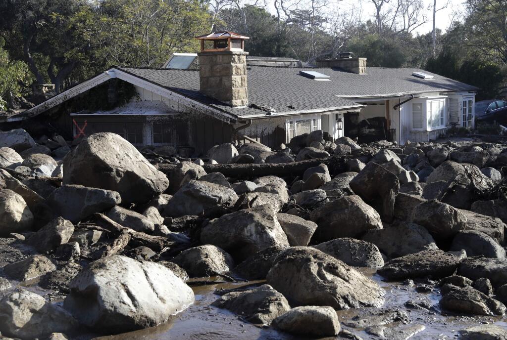 FILE - In this Jan. 11, 2018, file photo, large rocks and mud are shown in front of a house in Montecito, Calif. Local emergency authorities preparing for future storms like the one that devastated the Southern California community of Montecito with massive debris flows have eliminated the word 'voluntary' from language used in evacuation orders. (AP Photo/Marcio Jose Sanchez, File)
