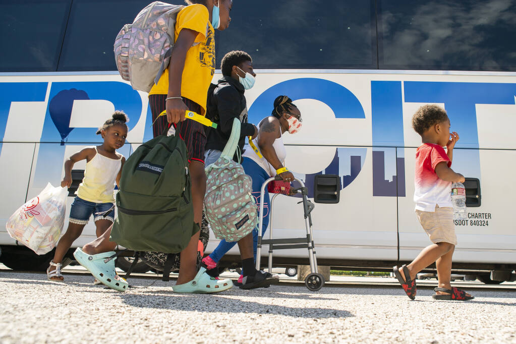 A family walks to a charter bus that will evacuate them from Galveston Island to Austin in anticipation of impact from Hurricane Laura, Tuesday, Aug. 25, 2020, at the Galveston Housing Authority offices in Galveston. (Mark Mulligan/Houston Chronicle via AP)