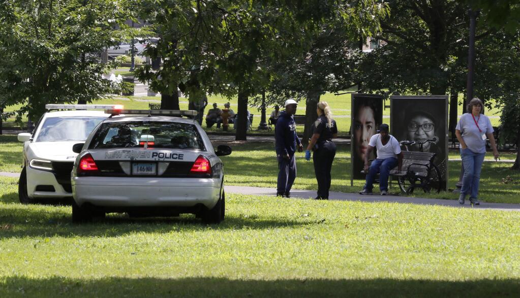 A police officer speaks to a man walking on New Haven Green, Wednesday, Aug. 15, 2018, in New Haven, Conn. A city official said more than a dozen people fell ill from suspected drug overdoses on the green and were taken to local hospitals. (AP Photo/Bill Sikes)