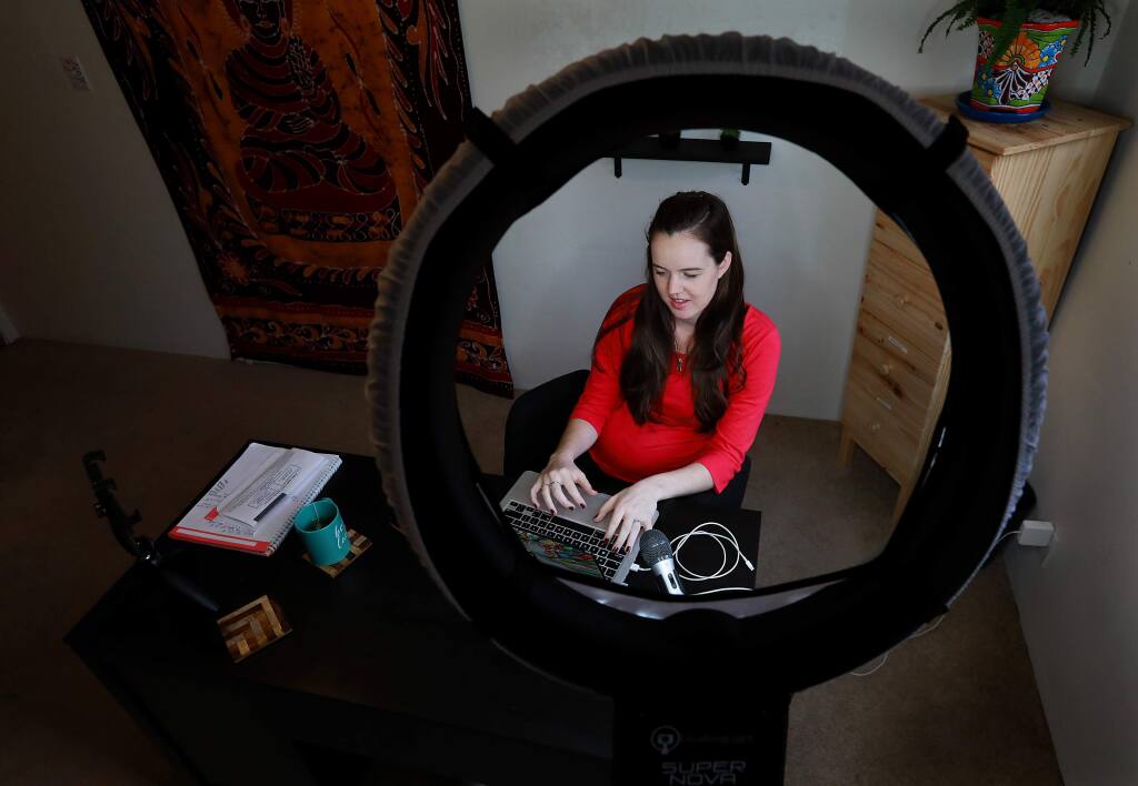 Emily Hirsh is a virtual assistant who helps small business owners with bulk email, Facebook ads and dealing with clients. She is seen in her Sebastopol home office through a light she uses for training videos. (John Burgess/The Press Democrat)