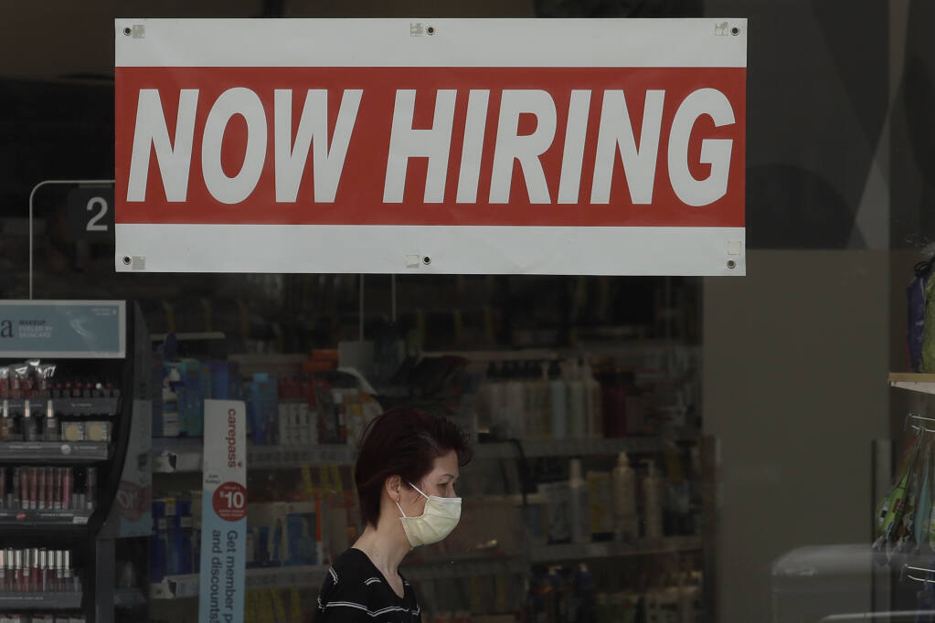 A woman wears a mask during the coronavirus outbreak while walking under a Now Hiring sign at a CVS Pharmac yin San Francisco, Thursday, May 7, 2020. (AP Photo/Jeff Chiu)