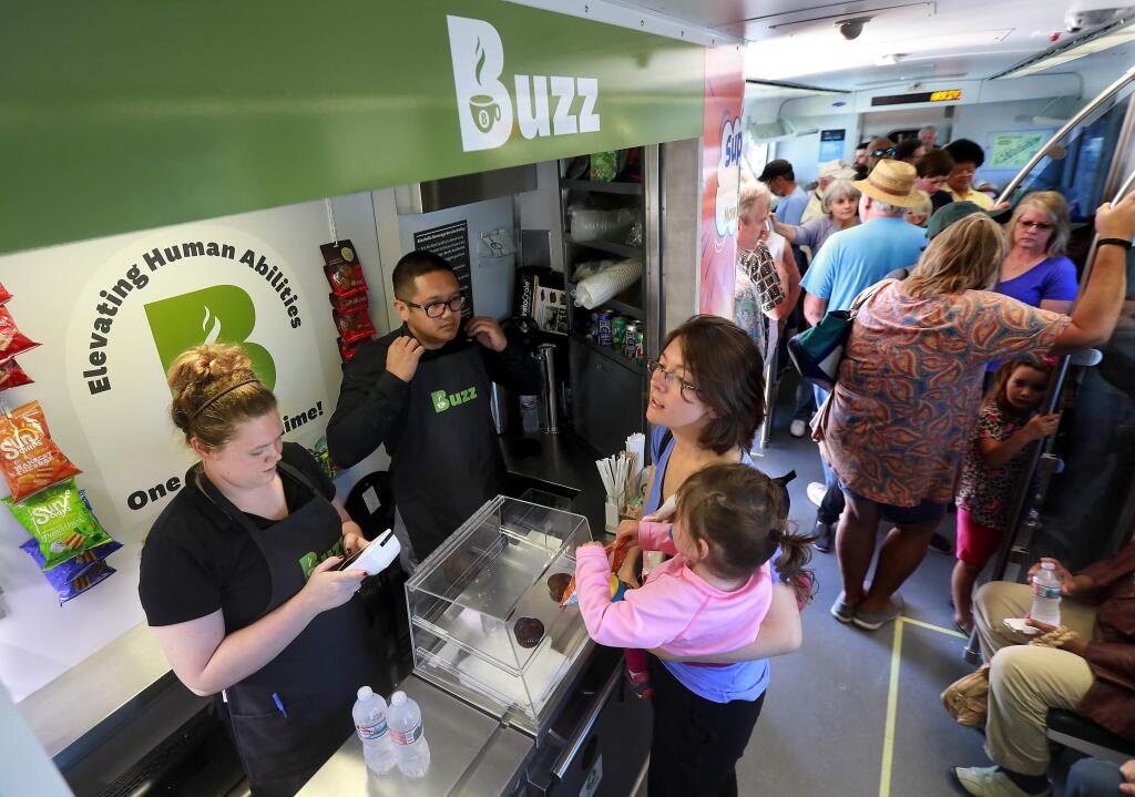 Michelle Stoffer of Corte Madera orders a snack for her daughter Nora, 2, from Meghan Harris and Jay Jay Rico on the SMART train during a free ride day on Thursday. (JOHN BURGESS / The Press Democrat)