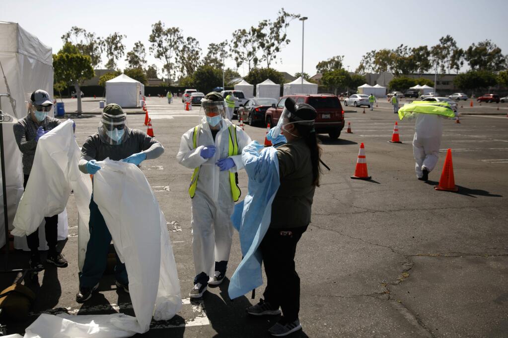A group of volunteers put on protective suits at a city-run, drive-thru COVID-19 testing site in South Central Los Angeles, Friday, May 22, 2020. (AP Photo/Jae C. Hong)