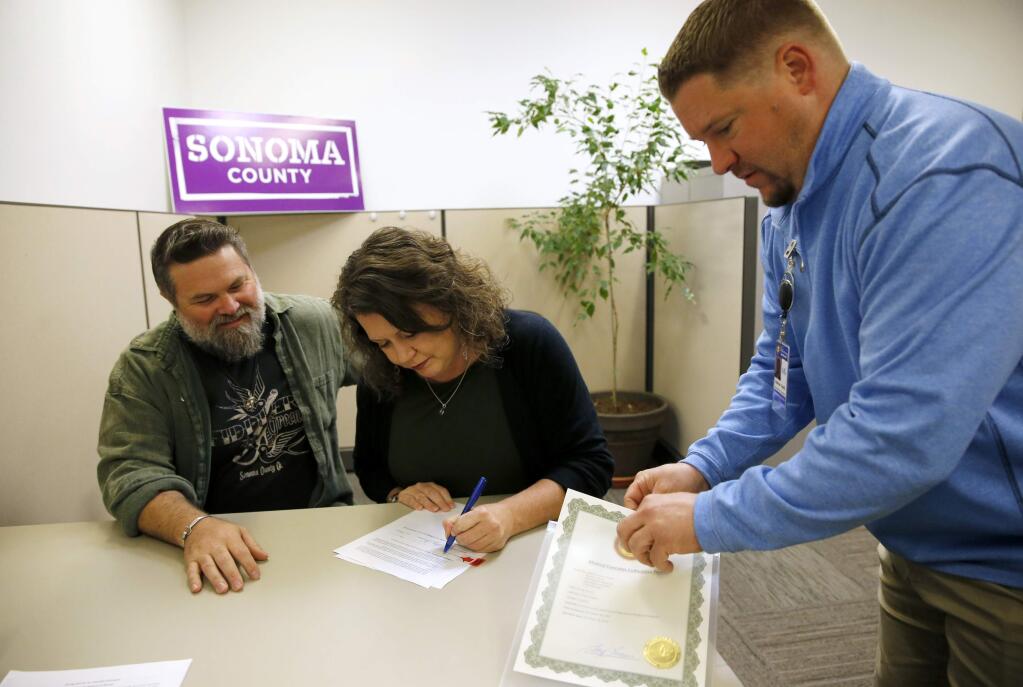 Fiddler's Greens co-owner Shannon Hattan, joined by her husband Cameron, left, and Andrew Smith, the Deputy Agricultural Commissioner, signs an approval letter for a zoning permit for cannabis cultivation at the Agricultural Commission office in Santa Rosa, on Monday, December 4, 2017. (BETH SCHLANKER/ The Press Democrat)