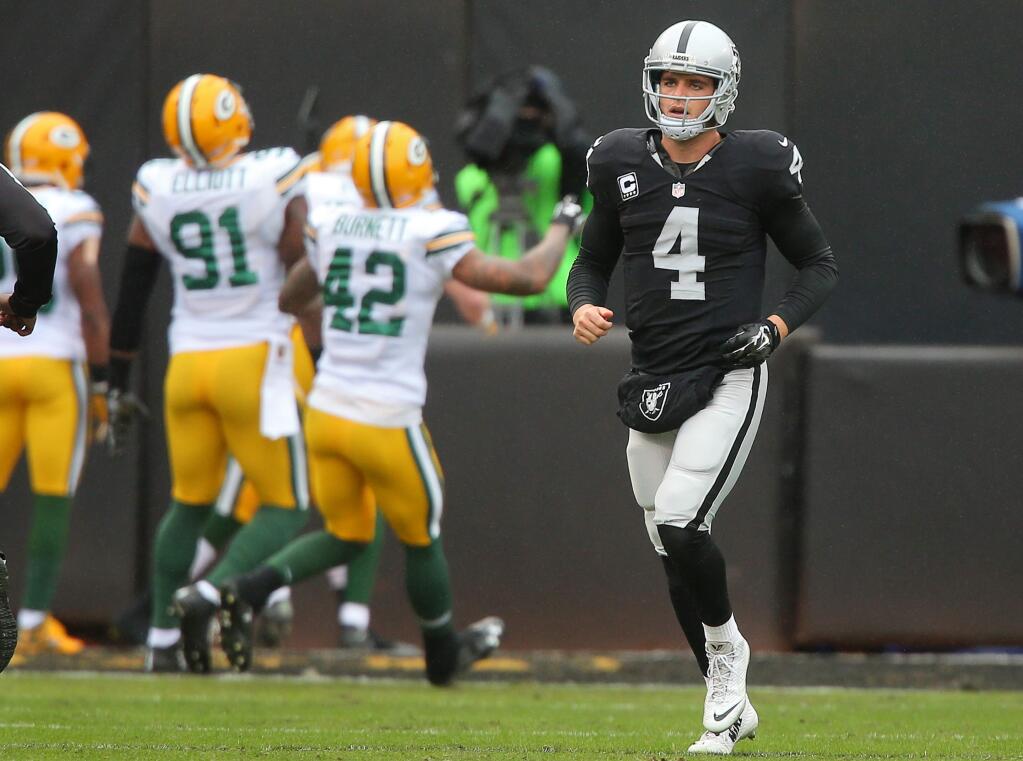 Oakland Raiders quarterback Derek Carr runs off the field as the Green Bay Packers celebrate after scoring on an interception, during their game in Oakland on Sunday, December 20, 2015. The Raiders lost to the Packers 30-20.(Christopher Chung/ The Press Democrat)