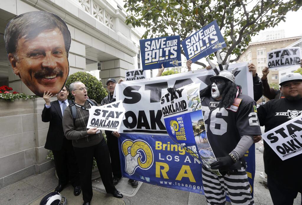 A photo of St. Louis Rams owner Stan Kroenke, left, is held up by Rams fans as they rally with San Diego Chargers and Oakland Raiders fans outside of the NFL's spring meetings in San Francisco, Tuesday, May 19, 2015. (AP Photo/Jeff Chiu)