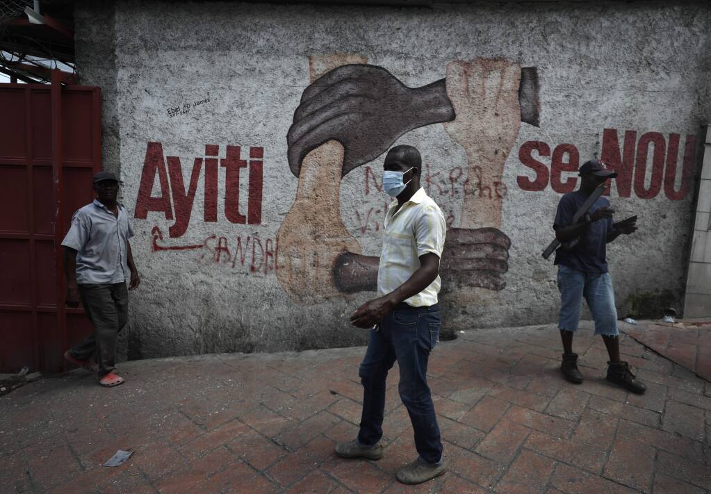 Demonstrators walk past a mural that reads in Creole 'Haiti is us' during anti-government protests in Port-au-Prince, Haiti, Friday, Oct. 11, 2019. Protesters burned tires and spilled oil on streets in parts of Haiti's capital as they renewed their call for the resignation of President Jovenel Moïse just hours after a journalist was shot to death. (AP Photo/Rebecca Blackwell)