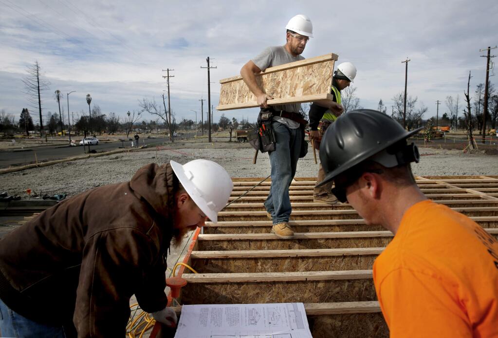 Rob Williams, left, a superintendent with Lake County Contractors, looks at building plans with plumber Tom Groff, right, as Jesse Merritt, center, carries a floor joist for installation as they rebuild a home on Kerry Lane in Coffey Park in Santa Rosa on Tuesday, Jan. 2, 2018. (BETH SCHLANKER/ PD)