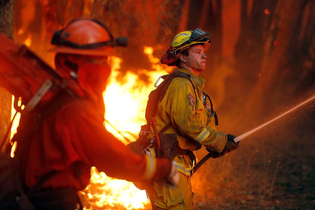 Cal Fire Siskyou firefighter Chance Jackson, right, cools down some burning vegetation during a firing operation at the Oakmont fire in Santa Rosa, California on Tuesday, October 17, 2017. (Alvin Jornada / The Press Democrat)
