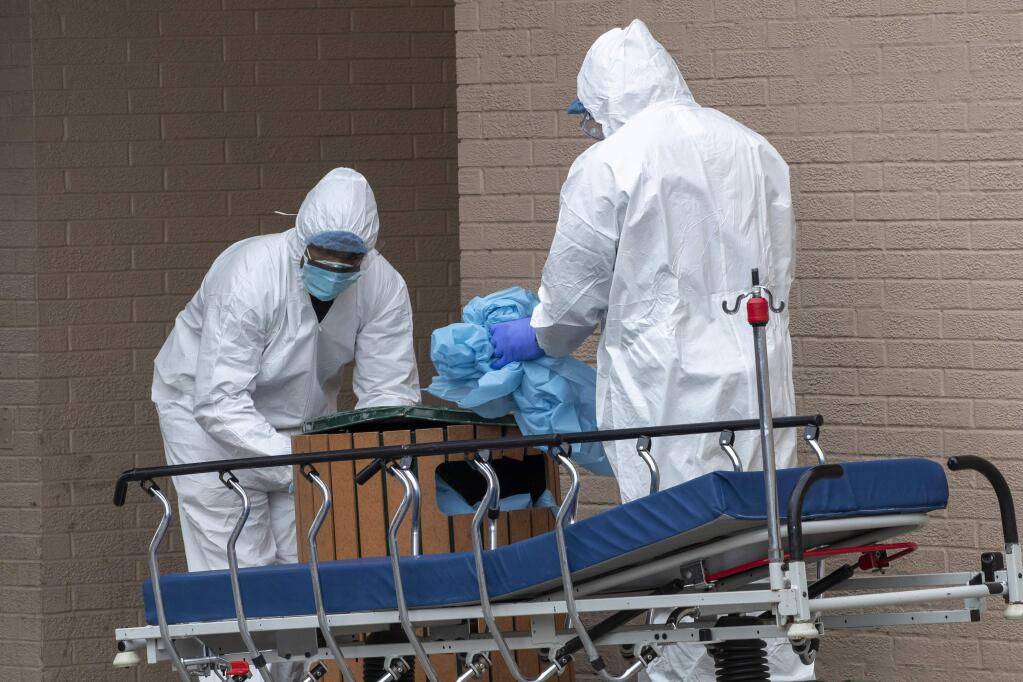 Medical personnel remove their personal protective equipment to protect against COVID-19, after delivering a bodies from the Wyckoff Heights Medical Center to refrigerated containers parked outside, Thursday, April 2, 2020 in the Brooklyn borough of New York. (AP Photo/Mary Altaffer)