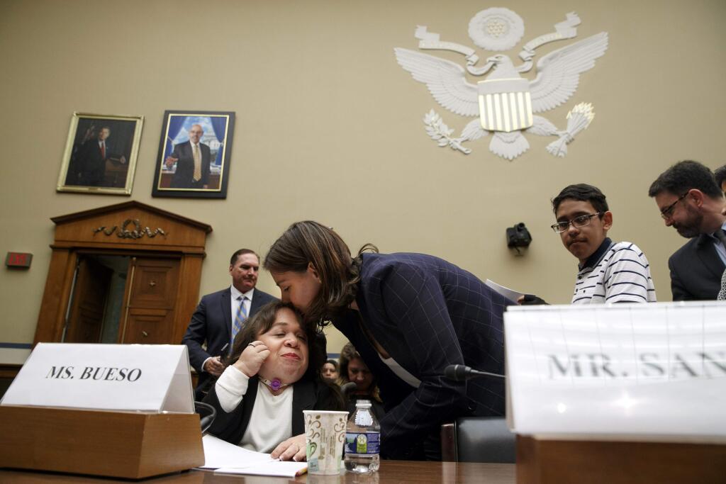 Maria Isabel Bueso, 24, of Concord, Calif., left, is kissed on the forehead for luck by her friend Carly Marcus, next to Jonathan Sanchez, 16, of Boston, before Bueso and Sanchez, testify at a House Oversight subcommittee hearing into the Trump administration's decision to stop considering requests from immigrants seeking to remain in the country for medical treatment and other hardships, Wednesday, Sept. 11, 2019, on Capitol Hill in Washington. (AP Photo/Jacquelyn Martin)