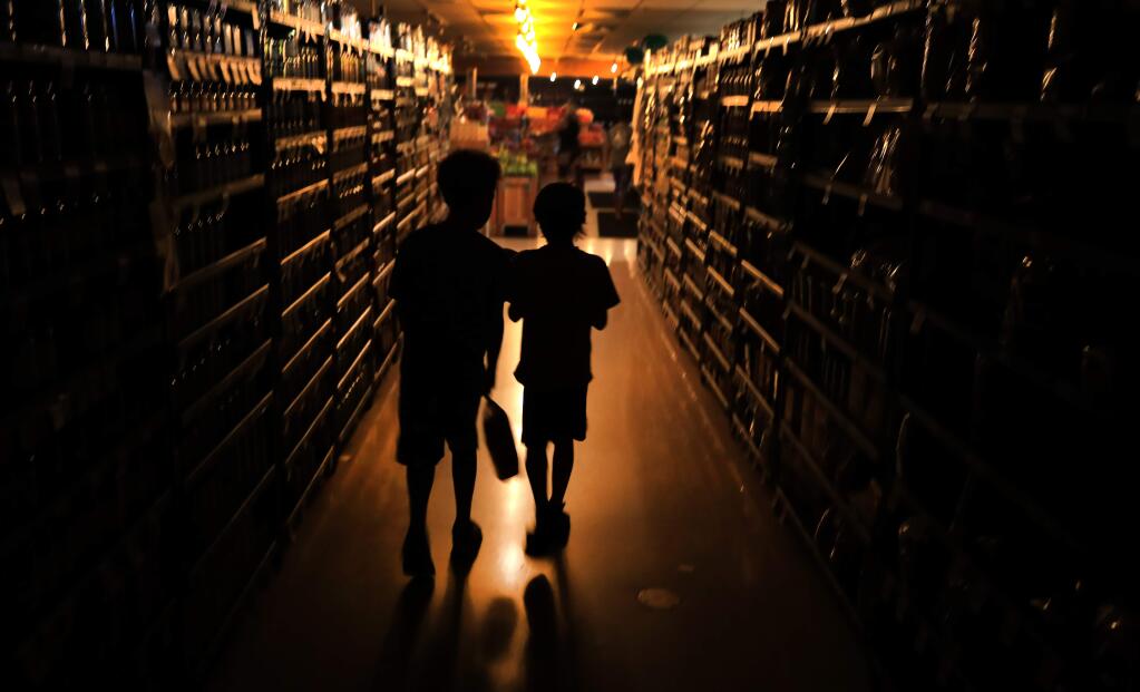 Elijah Carter 11, left, and Robert Haralson, 12, help shop for their parents in a darkened Olivers Supermarket in Rincon Valley, Wednesday, Oct. 23, 2019. The west side of the store was lit by patio lights powered by a generator as power was shut off again by PG&E due to fire danger. (Kent Porter / The Press Democrat file)