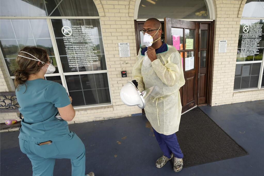 Dr. Robin Armstrong, right, adjusts his mask outside the entrance to The Resort at Texas City nursing home, where he is the medical director, Tuesday, April 7, 2020, in Texas City, Texas. Armstrong is treating nearly 30 residents of the nursing home with the anti-malaria drug hydroxychloroquine, which is unproven against COVID-19 even as President Donald Trump heavily promotes it as a possible treatment. Armstrong said Trump's championing of the drug is giving doctors more access to try it on coronavirus patients. More than 80 residents and workers have tested positive for coronavirus at the nursing home. (AP Photo/David J. Phillip)