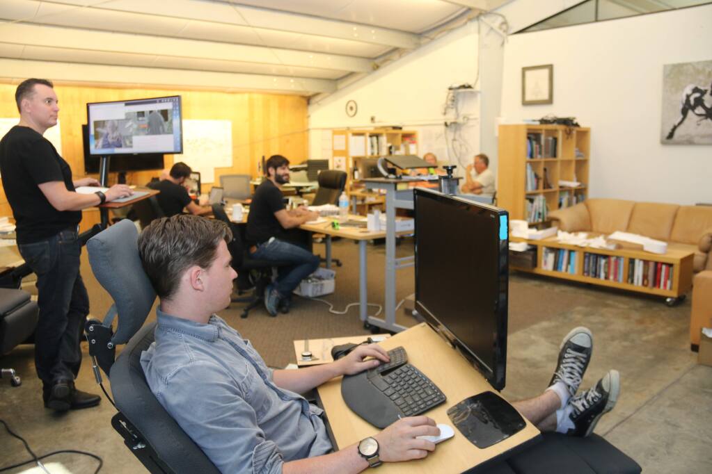 Intern Maxwell Adam demonstrates the sitting position of the Altwork workstation with extended footrest at the company's development 'barn' near Geyserville in northern Sonoma County on Aug. 10, 2016. Co-founder and CEO Che Voigt, left, shows how the workstation converts to a standing desk. (JEFF QUACKENBUSH / NORTH BAY BUSINESS JOURNAL)