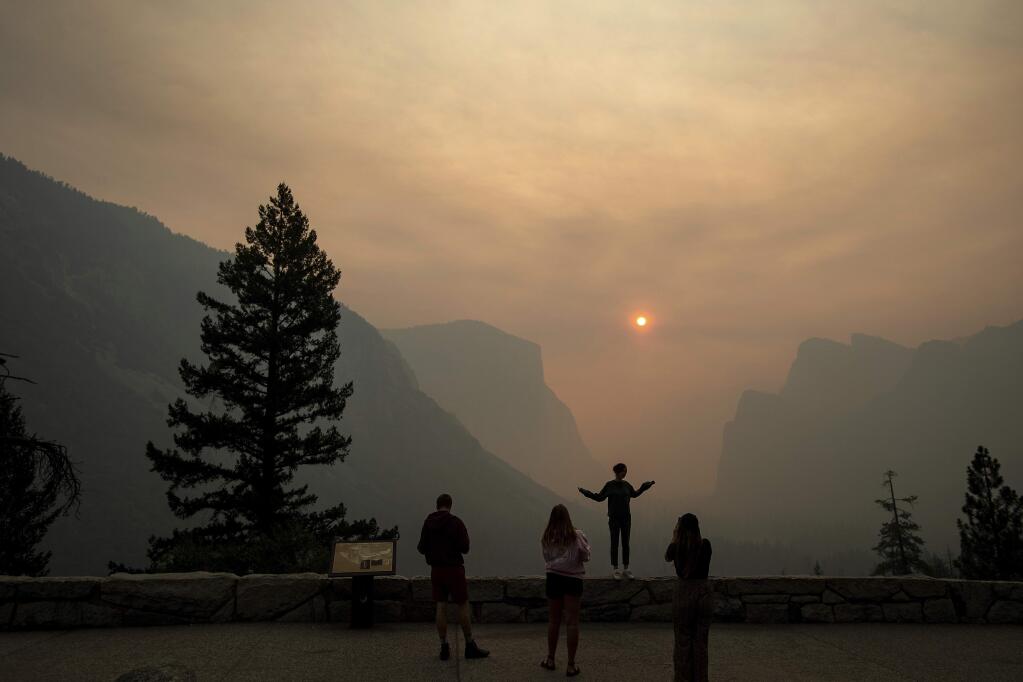 FILE - In this July 25, 2018 file photo, Hannah Whyatt poses for a friend's photo as smoke from the Ferguson fire fills Yosemite Valley in Yosemite National Park, Calif. Yosemite National Park could reopen its scenic valley and other areas Monday, Aug. 6, 2018, if conditions improve after a 12-day closure due to nearby wildfires. The park's iconic cliffs have been shrouded in so much smoke that the air quality in Yosemite is currently worse than Beijing. (AP Photo/Noah Berger, File)