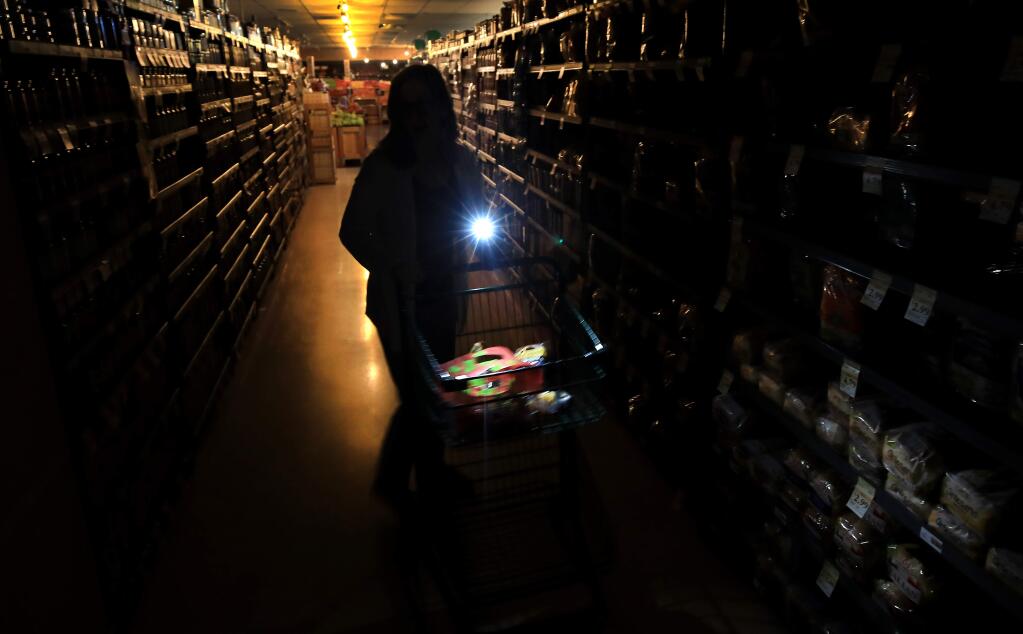 Suzanne Allen shops in a darkened Oliver's Supermarket in Rincon Valley, Wednesday, Oct. 23, 2019. The west side of the store was lit by patio lights powered by a generator as power was shut off again by PG&E due to fire danger. (KENT PORTER/ PD)