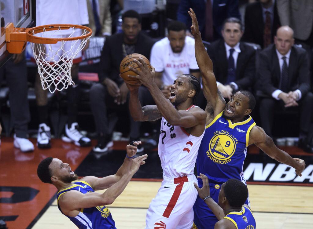 Toronto Raptors forward Kawhi Leonard (2) knocks down Golden State Warriors guard Stephen Curry, left, as he drives to the net past Golden State Warriors guard Andre Iguodala (9) during the first half of Game 1 of basketball‚Äôs NBA Finals, Thursday, May 30, 2019, in Toronto. (Nathan Denette/The Canadian Press via AP)
