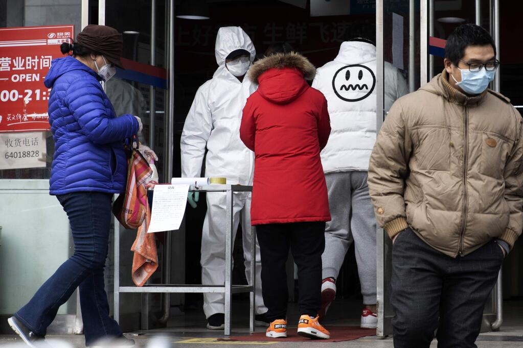 FILE - In this Thursday, Feb. 27, 2020, file photo, a worker in overalls screen for fever at the entrance to a supermarket in Beijing. Health officials reported the first U.S. drug shortage tied to the viral outbreak that is disrupting production in China, but they declined to identify the manufacturer or the product. The Food and Drug Administration said late Thursday, that the drug's maker contacted health officials recently about the shortage, which it blamed on a manufacturing issue with the medicine's key ingredient. (AP Photo/Ng Han Guan, File)