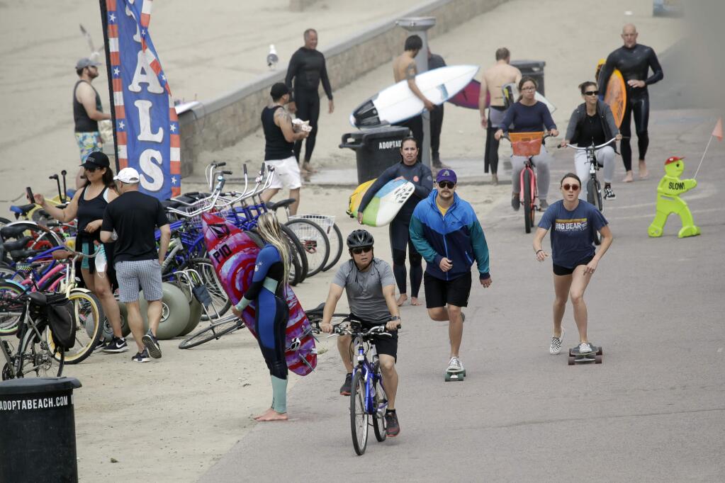 Bikers, walkers, skaters and surfers crowd a paved trail along the beach Sunday, April 26, 2020, in Huntington Beach, Calif. A lingering heat wave lured people to California beaches, rivers and trails again Sunday, prompting warnings from officials that defiance of stay-at-home orders could reverse progress and bring the coronavirus surging back. (AP Photo/Marcio Jose Sanchez)