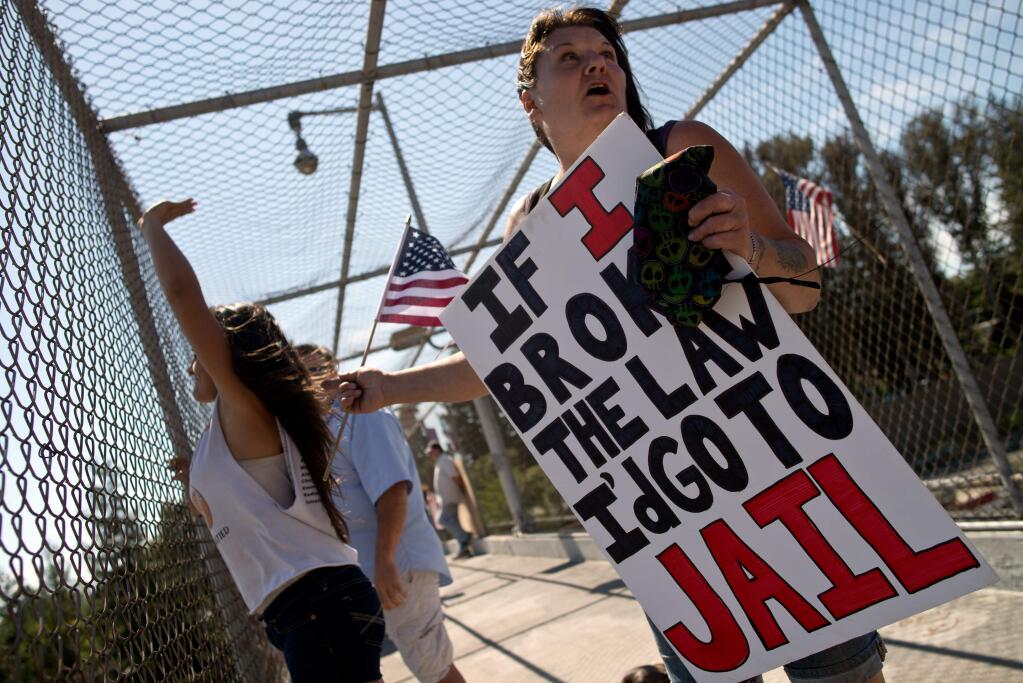Standing on a pedestrian overcrossing above Highway 101, Alex Morrow, right, holds a protest sign as her granddaughter Alexis Mautner, 13, waves to passing motorists honking their horns in support of a demonstration calling for changes to immigration policy in Santa Rosa, California, on July 19, 2014. (Alvin Jornada / For The Press Democrat)